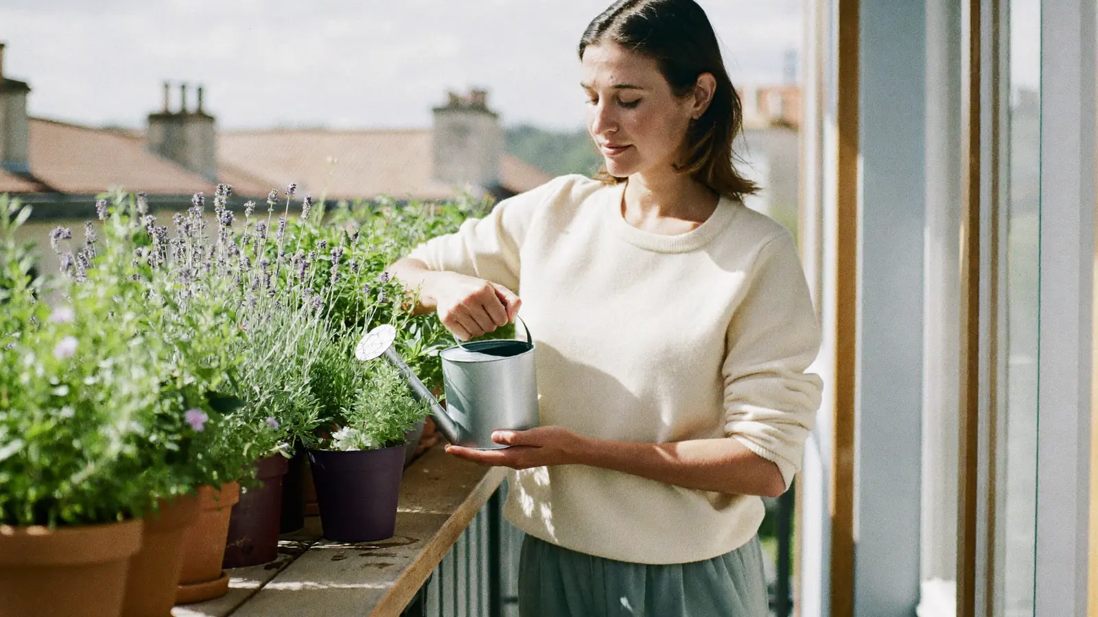 Une femme arrose des pots d'herbes aromatiques et de lavande sur un balcon ensoleillé, l'air paisible